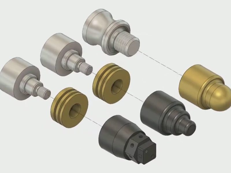 An exploded CAD view of turned components: stepped shafts with
                      threaded and ball ends, grooved brass spacers, and a bored housing,
                      laid out along two assembly axes.