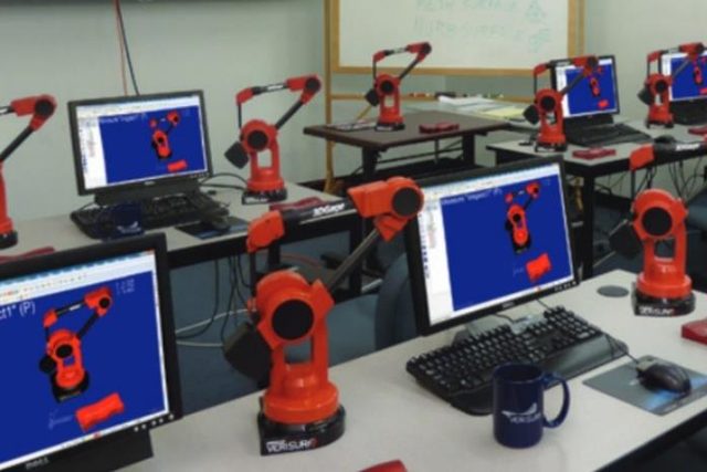 A classroom laid out as a metrology lab: rows of desks, each with a
                      3D Gage portable measuring arm beside a monitor running Verisurf
                      inspection software.